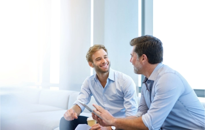 An experienced entrepreneur sits on a couch with a smiling young business owner during their mentorship session.