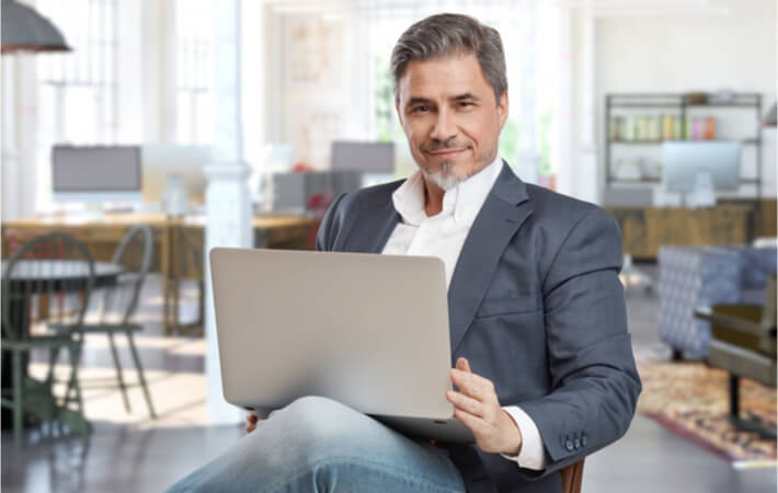 A confident and well dressed entrepreneur sitting in a chair and smiling while working on his computer.