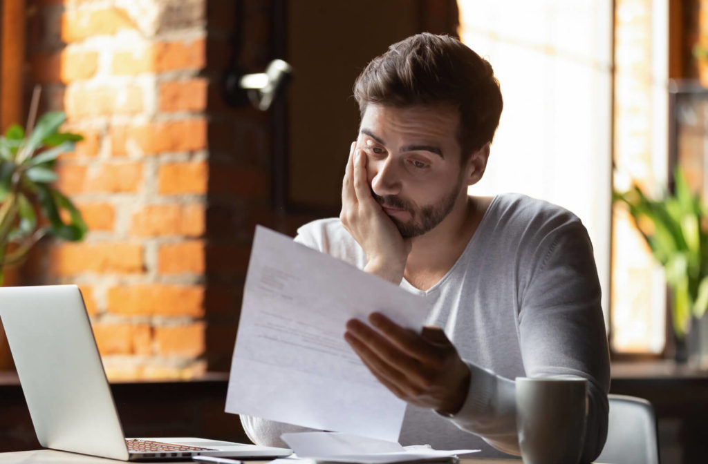 A young business owner appears stressed as he looks at a letter while working on his computer.